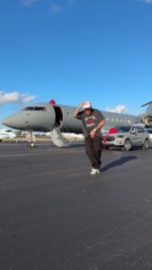 Man dancing in front of a private jet and SUV.