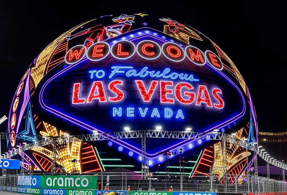 Race car driving past a sphere displaying a "Welcome to Fabulous Las Vegas" sign.