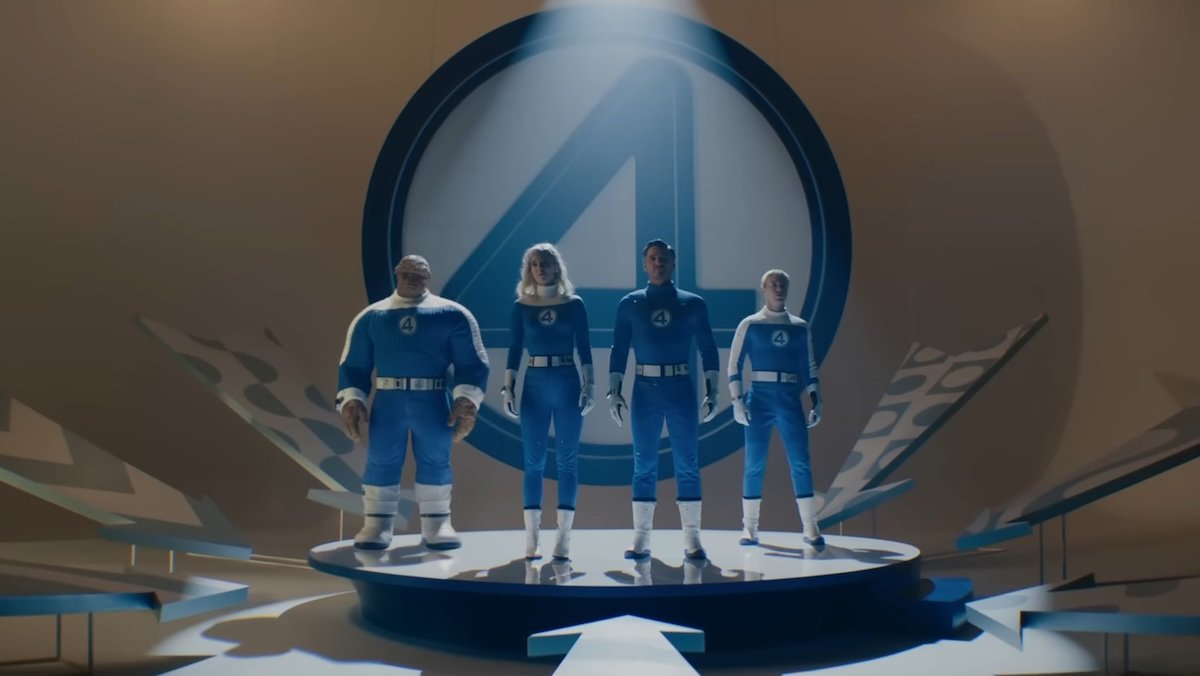 The Fantastic Four in their bleu and white suits on a stage with their 4 logo behind them