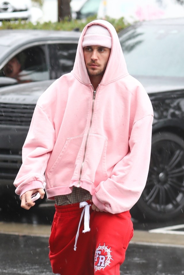 Justin Bieber wearing a pink hoodie and red sweatpants in the rain.