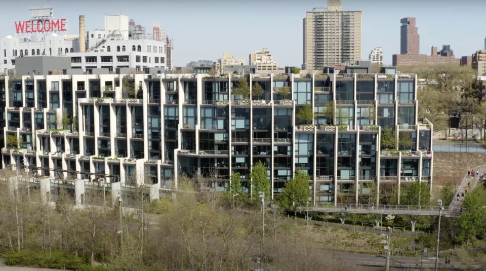 Aerial view of a modern apartment building with a walkway and surrounding park.