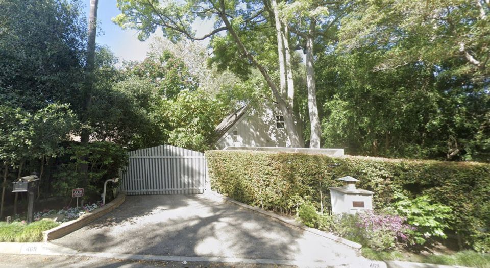 Driveway entrance to a house with a white gate and tall hedges.