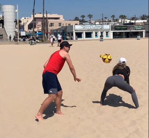 a man and a woman play volleyball on a beach in front of a building that says cool stuff