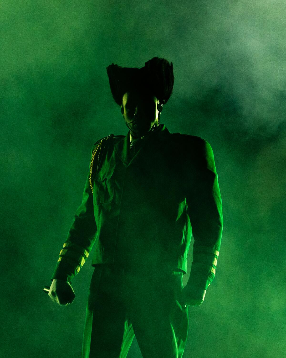 Lighting casts a green glow on Tyler, the Creator as he stands against a smoky green background