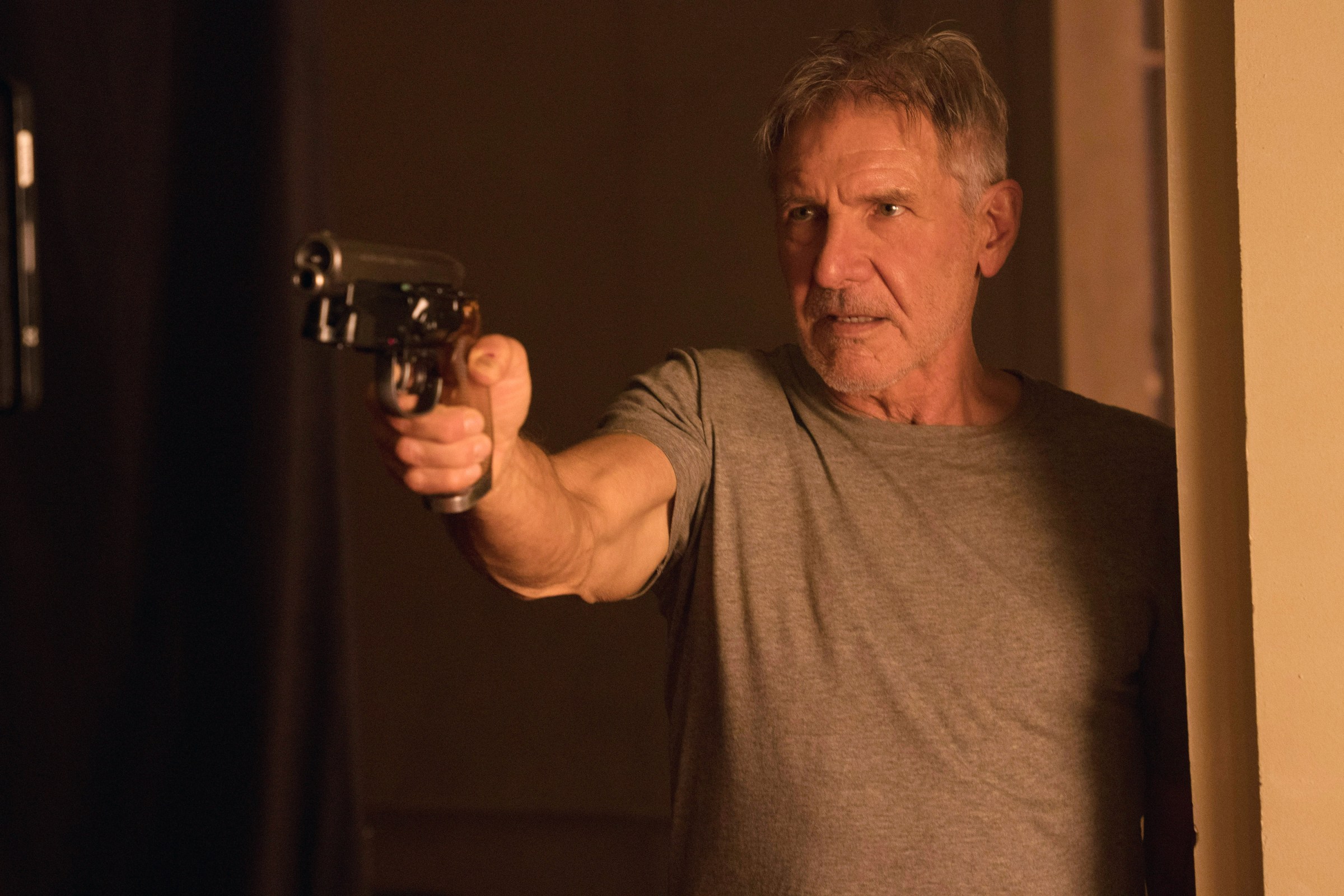 Harrison Ford standing in a doorway holding a futuristic pistol in Blade Runner 2049