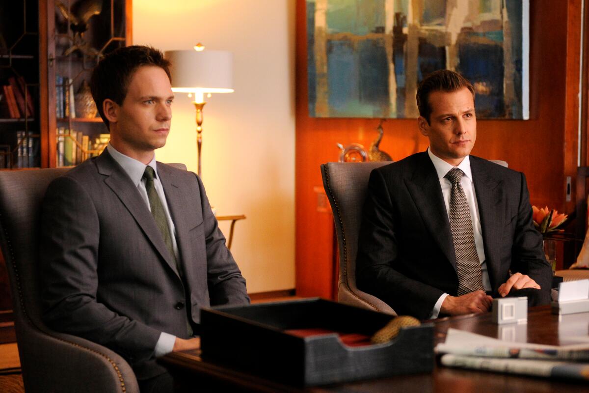 Two men wearing suits sit side by side