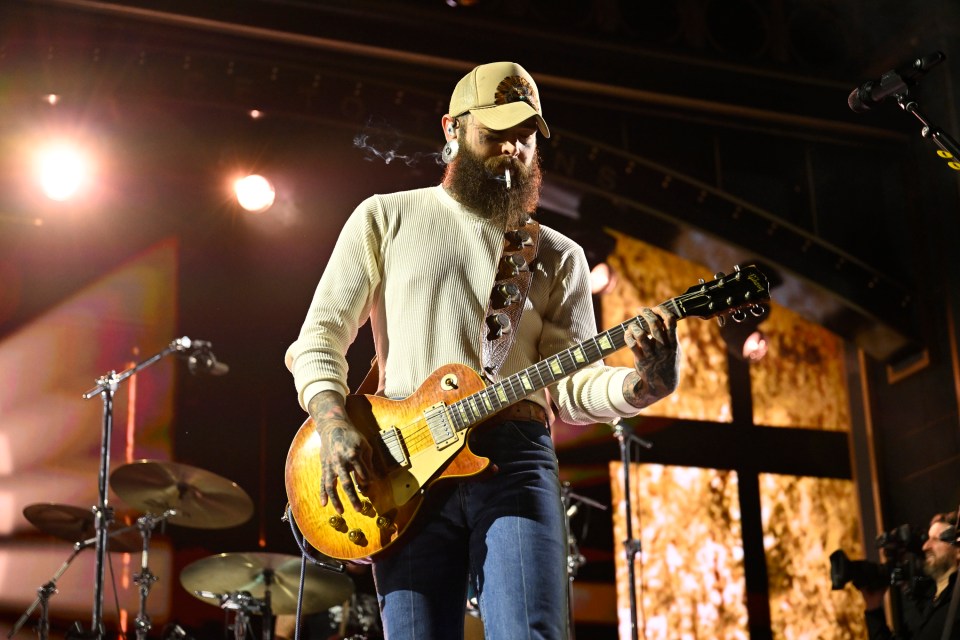 Post Malone performing on stage with a guitar.