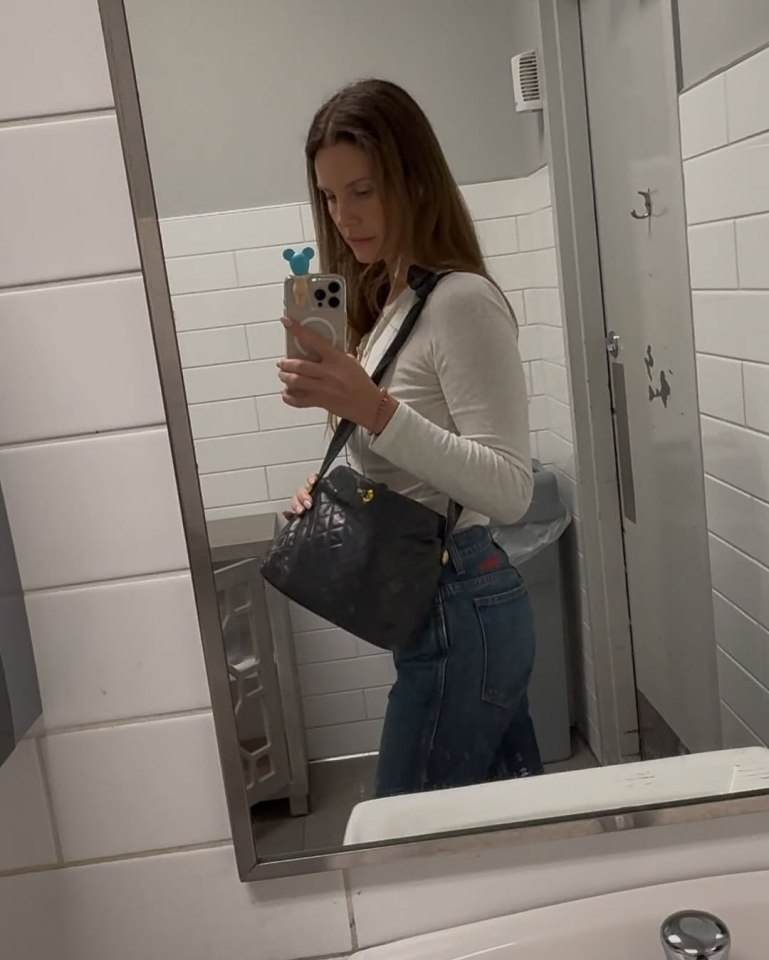 Woman in a restroom mirror taking a selfie.