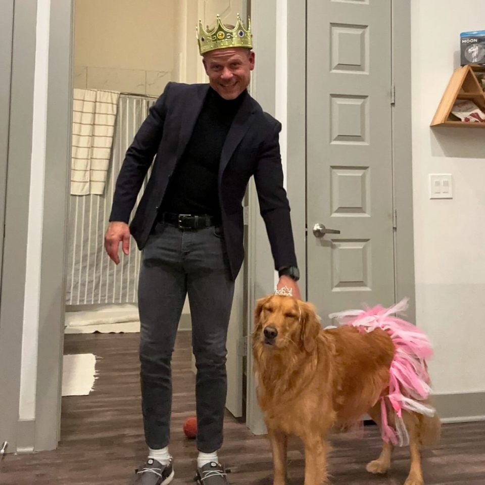 Man in a crown with his dog wearing a tutu.