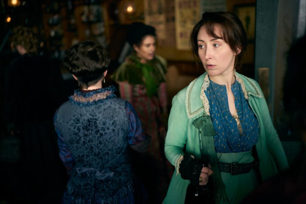 A woman in a green coat and blue shirt walks past women in a room.