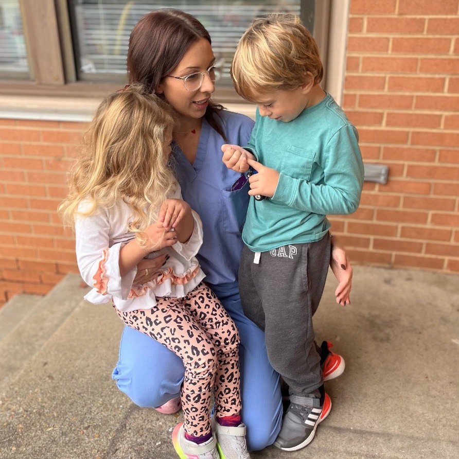 Woman kneeling and holding two young children.