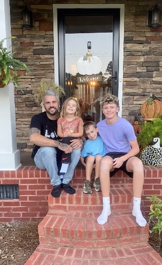 A man and three children sit on their front steps.