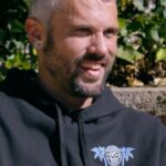 Man with gray hair smiling while wearing a black hoodie.