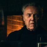 Christopher Walken in black at his dinner table in front of a fireplace on Severance