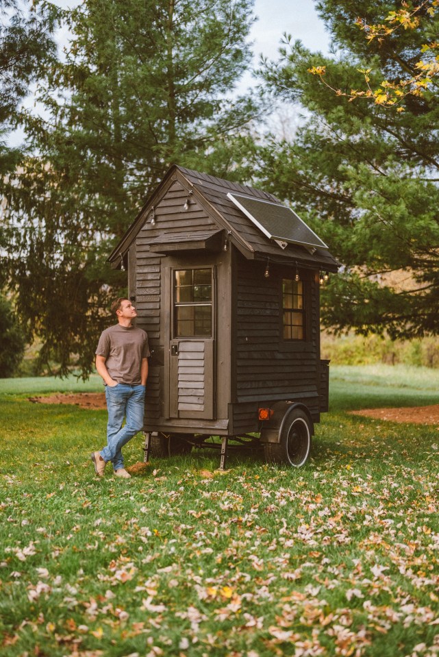 Man standing next to his tiny house with solar panels.