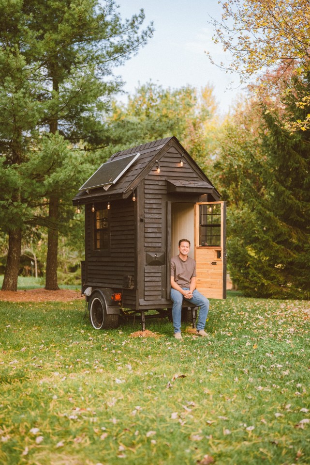 Man sitting outside his tiny house on wheels.