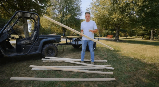 Man holding a long piece of lumber near a utility vehicle and a pile of lumber.