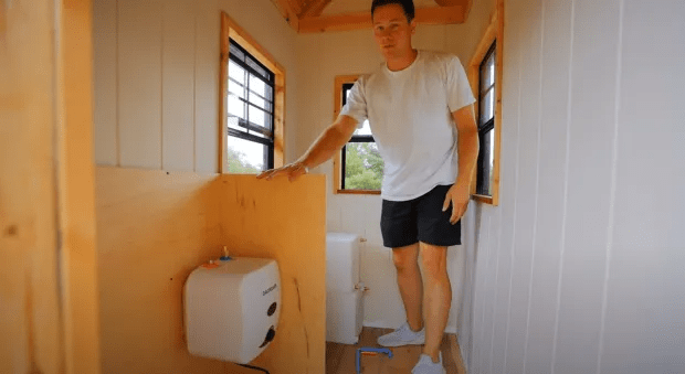 Man standing in small room with water heater and toilet.