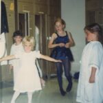 Four young girls in dresses in a locker room.