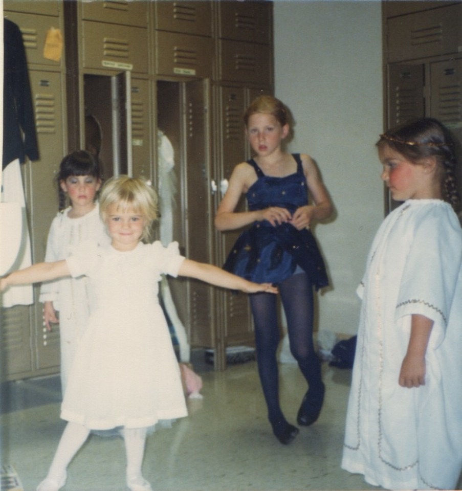 Four young girls in dresses in a locker room.