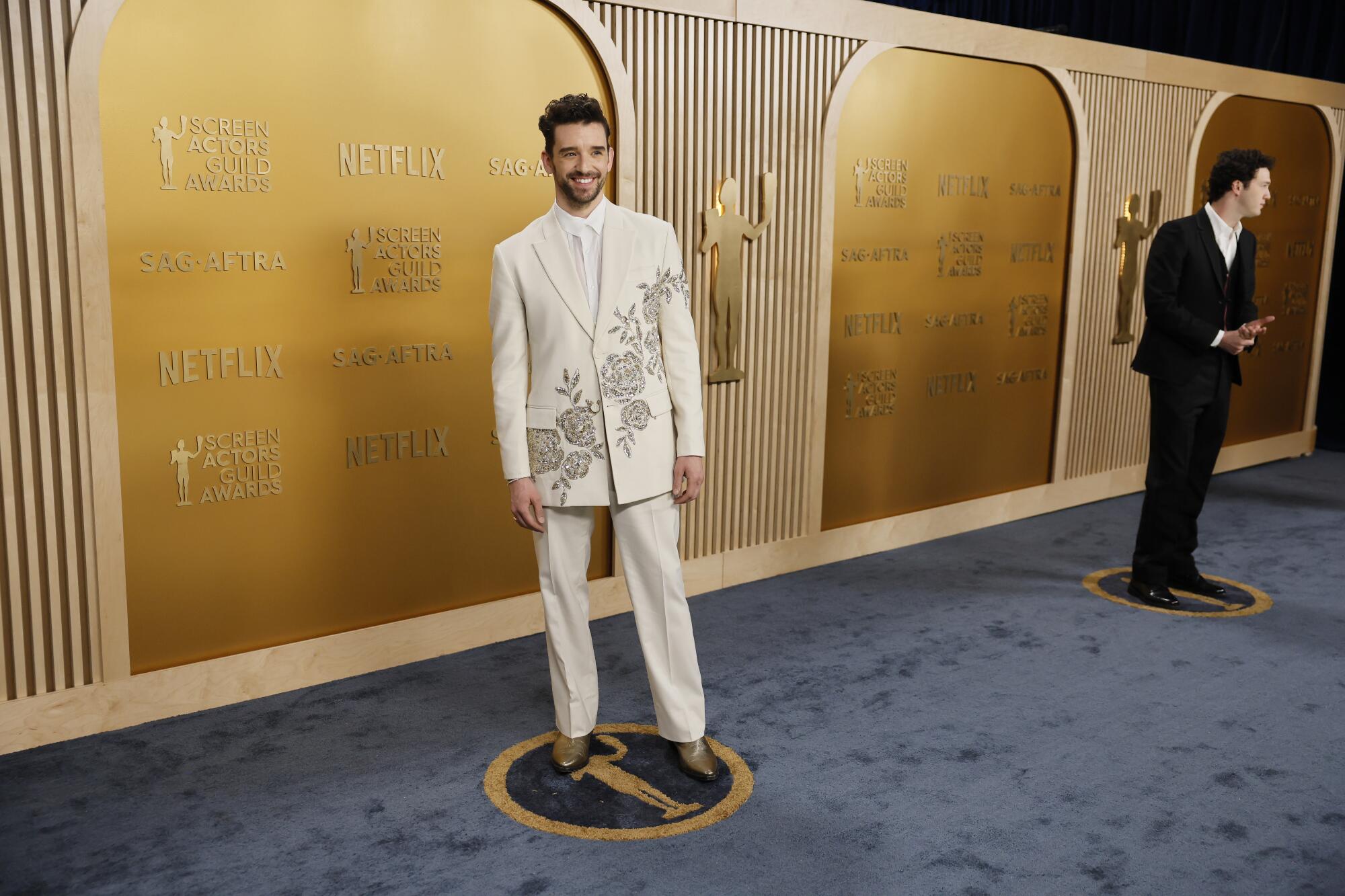 Michael Urie, in a bedazzled white suit, smiles at cameras. 