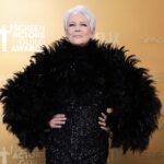 Jamie Lee Curtis, in a black beaded gown and feather boa, smiles at cameras.