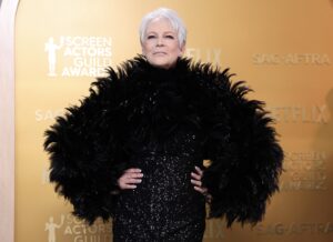 Jamie Lee Curtis, in a black beaded gown and feather boa, smiles at cameras.