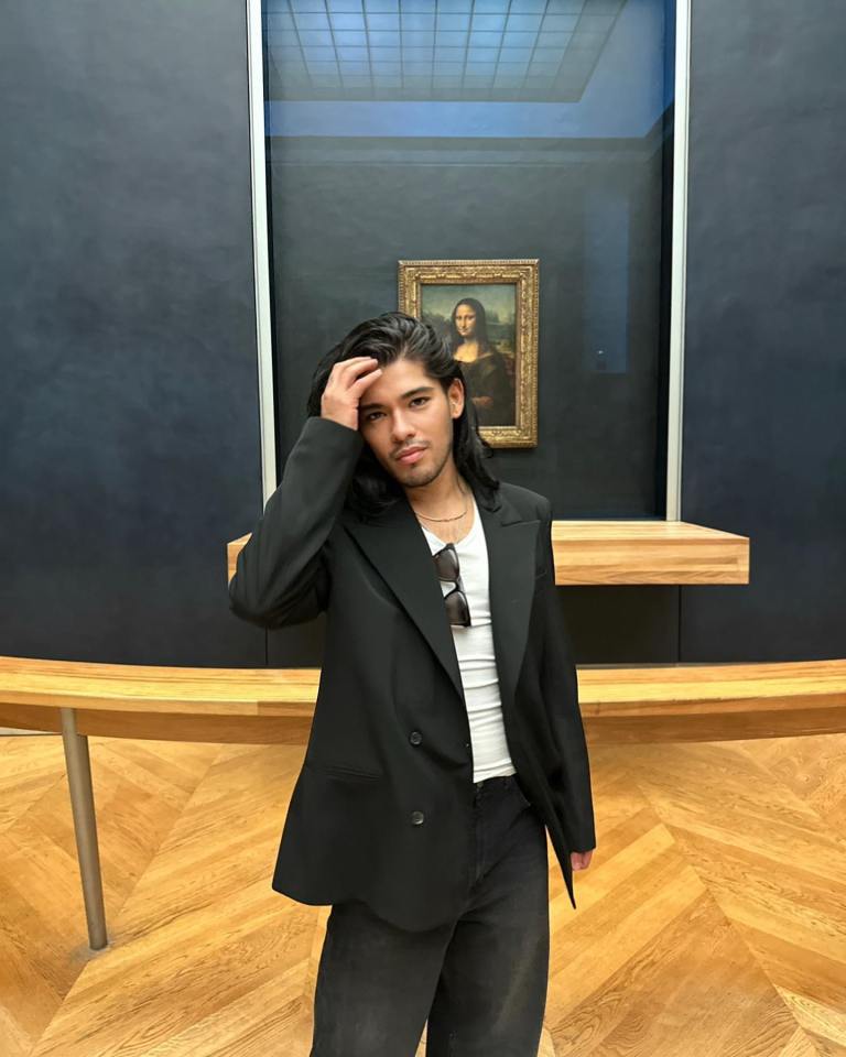 Man in black blazer standing in front of the Mona Lisa.