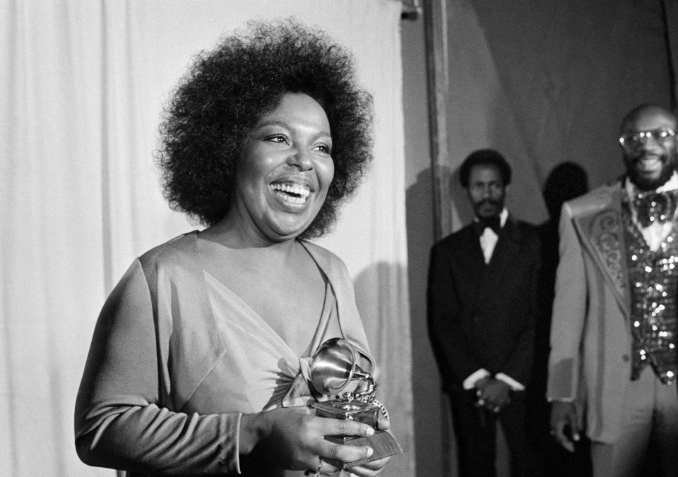 Roberta Flack holding a Grammy award with Isaac Hayes in the background.