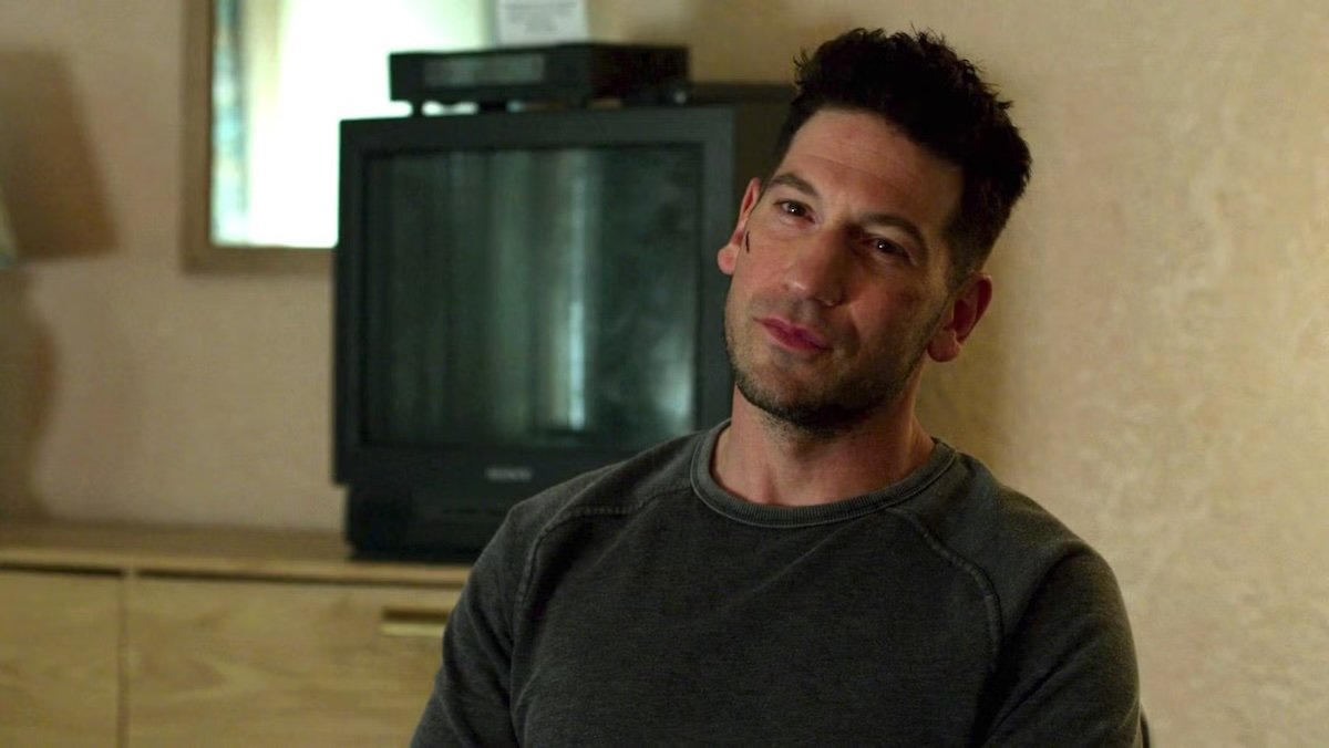 Jon Bernthal as Frank Castle sitting in a hotel room in front of a TV