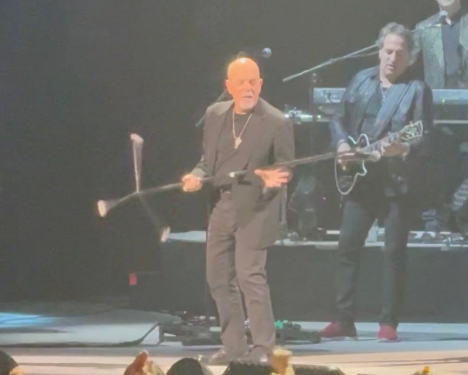 Billy Joel spinning a microphone stand on stage.