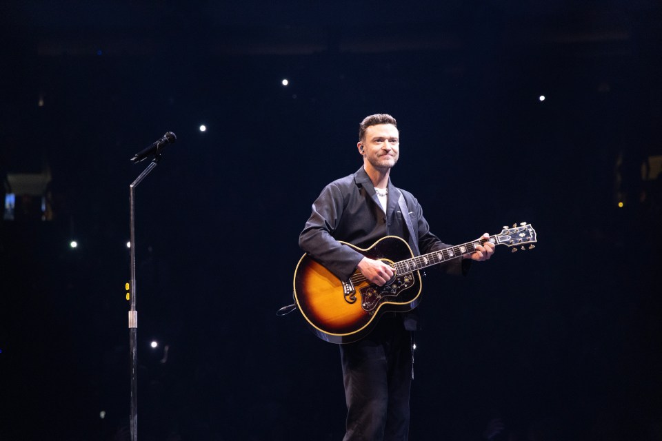 Justin Timberlake performing on stage with an acoustic guitar.