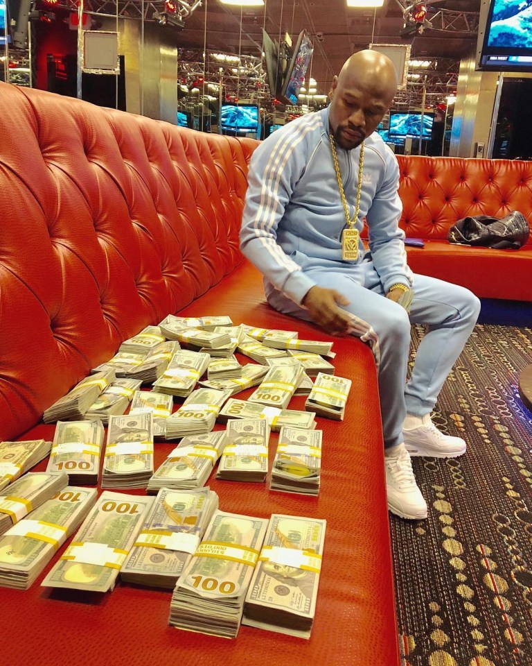 Floyd Mayweather sitting on a red couch with stacks of $100 bills.