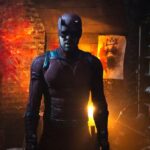 Daredevil stands in a dimly lit cellar with demonic images