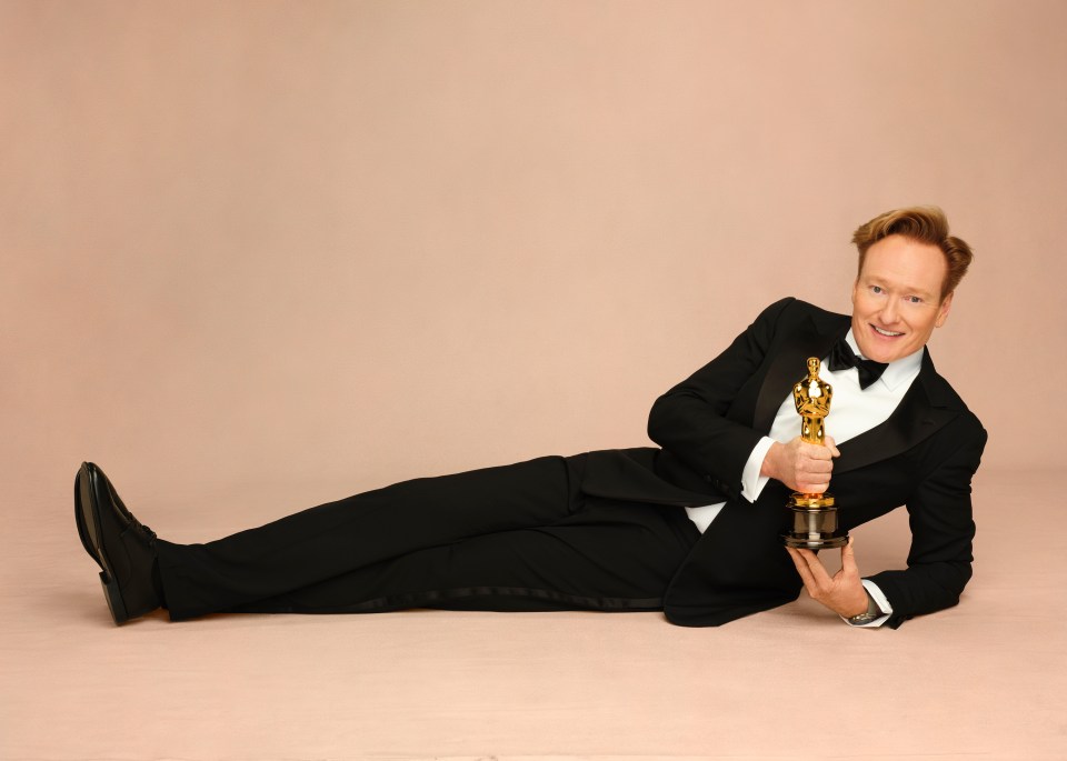 Conan O'Brien lying down holding an Oscar.