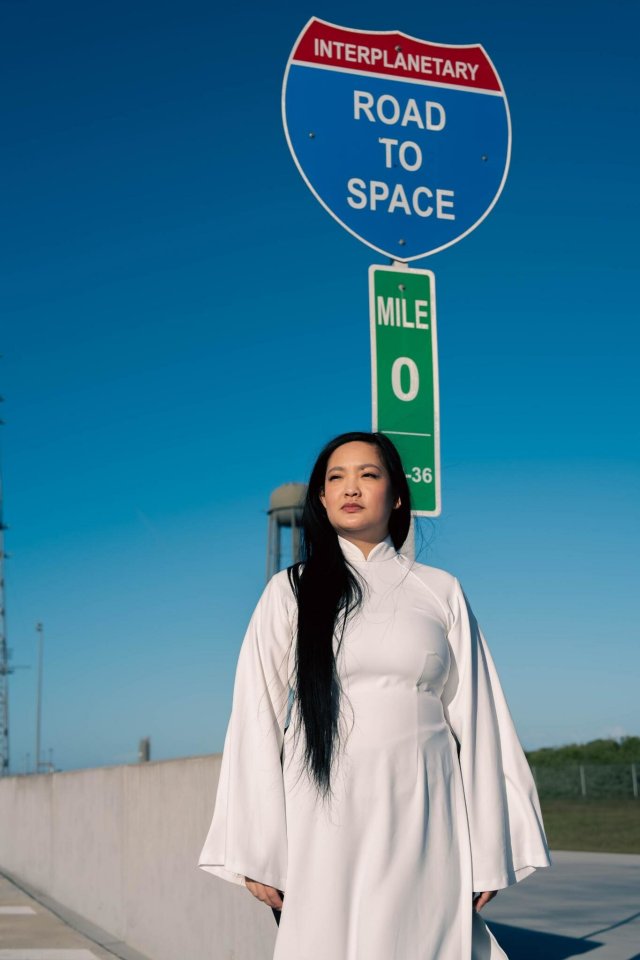 Woman in white dress standing under "Interplanetary Road to Space" sign.