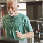 Senior man running on treadmill while listening to music