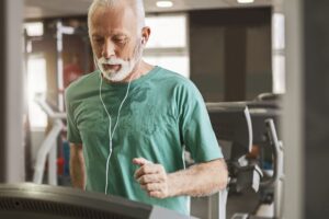 Senior man running on treadmill while listening to music