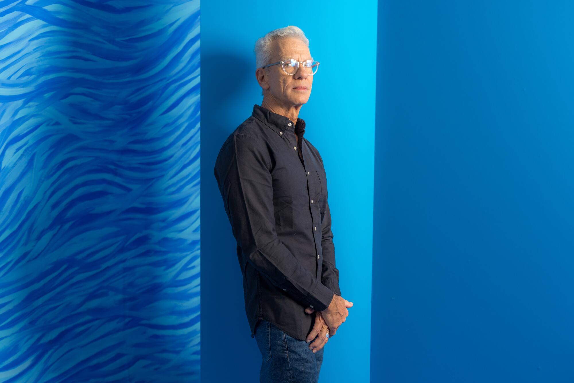  Chris Sanders stands in front of a bright blue wall for a portrait. 