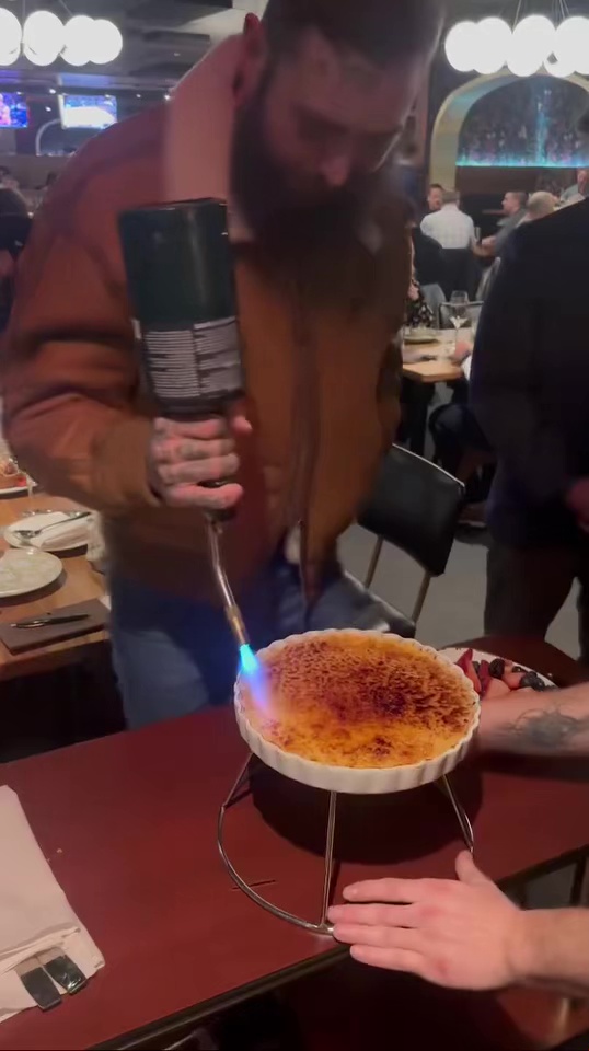 A man flambés a crème brûlée with a kitchen torch.