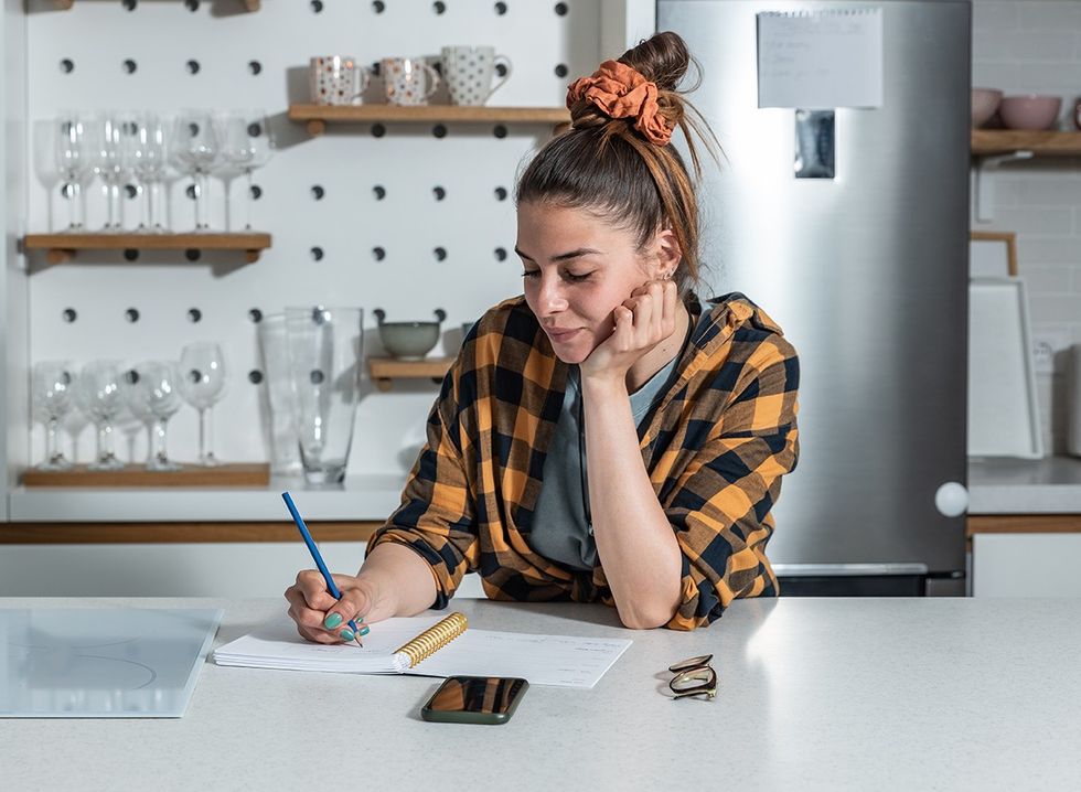 A woman in her kitchen making a grocery list