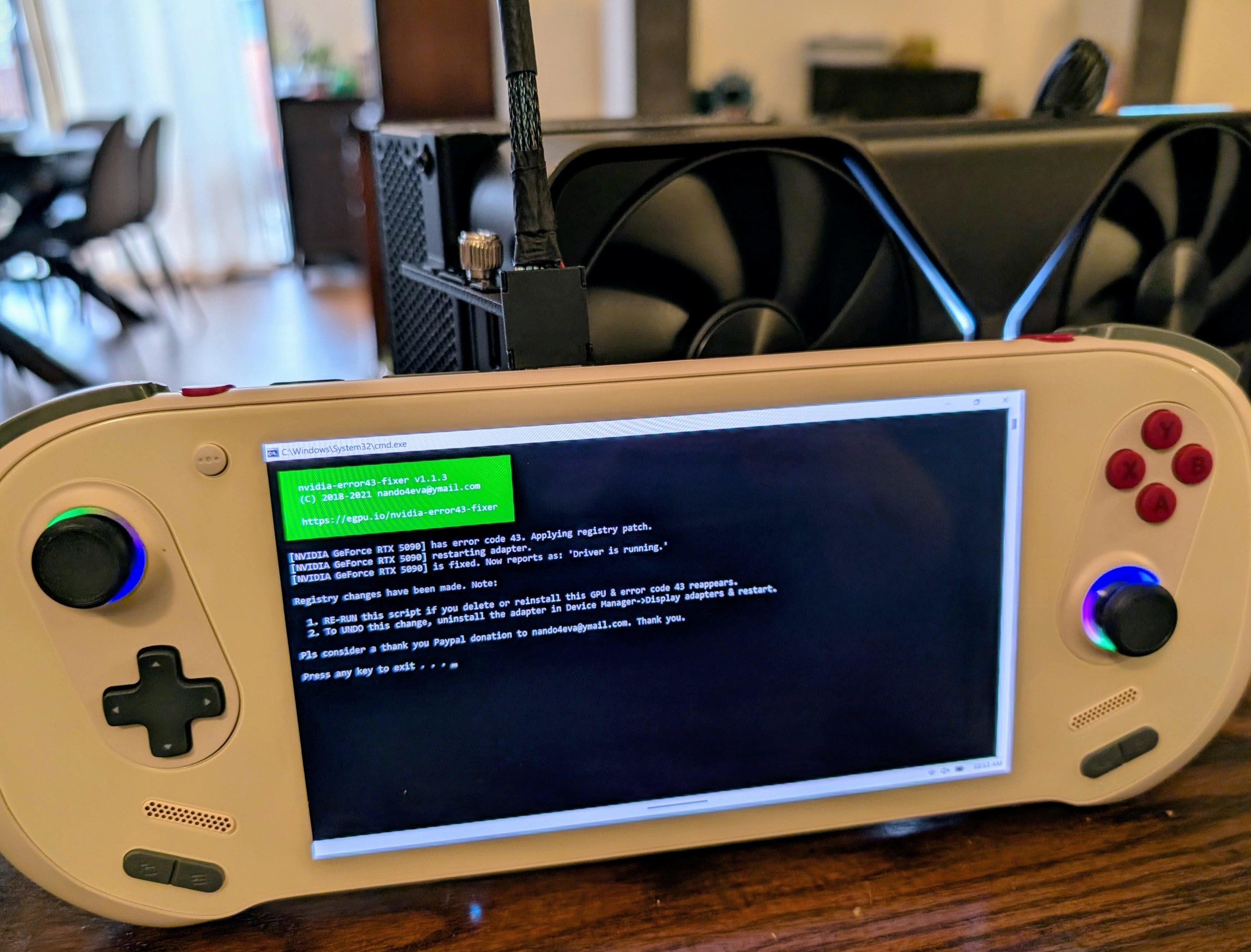 A beige gaming handheld plugged into a big GPU by a wide braided cover cable.