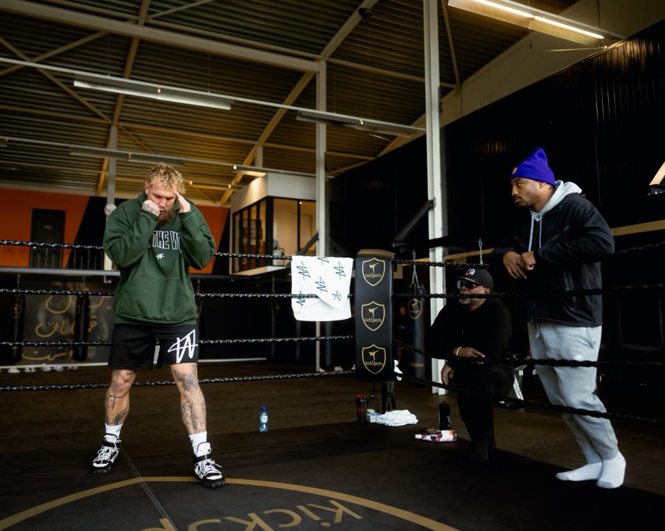 A boxer shadowboxing in a gym, watched by two men.