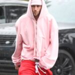 Justin Bieber wearing a pink hoodie and red sweatpants in the rain.