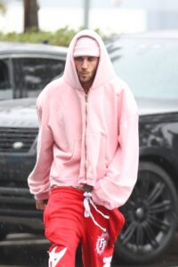 Justin Bieber wearing a pink hoodie and red sweatpants in the rain.