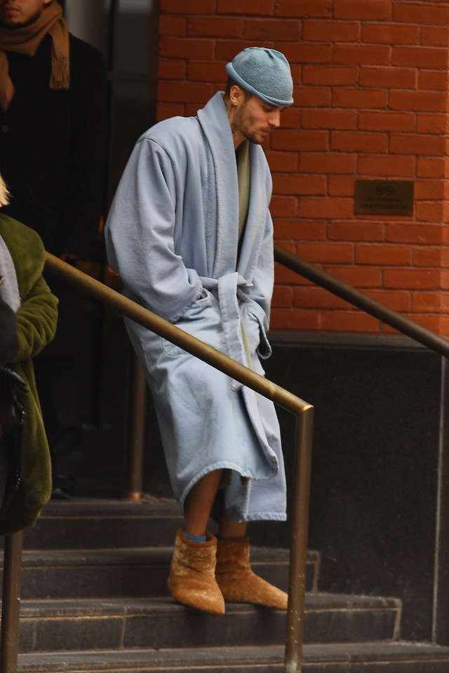 Justin Bieber in a light blue robe and brown slippers descending a staircase.