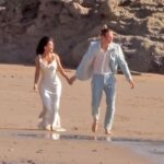 Kim Kardashian and Matthew Noszka on a beach, holding hands, in wedding attire.