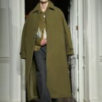 Model walking the runway in an olive green overcoat.