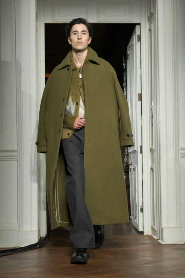 Model walking the runway in an olive green overcoat.