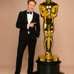 Conan O'Brien in a tuxedo pointing at an Oscar statuette.